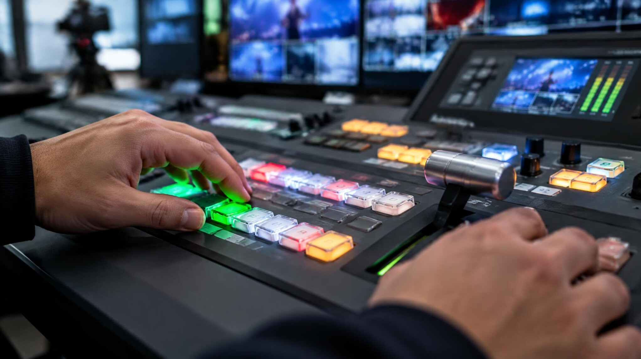 Close-up of hands operating a video switcher panel with glowing buttons